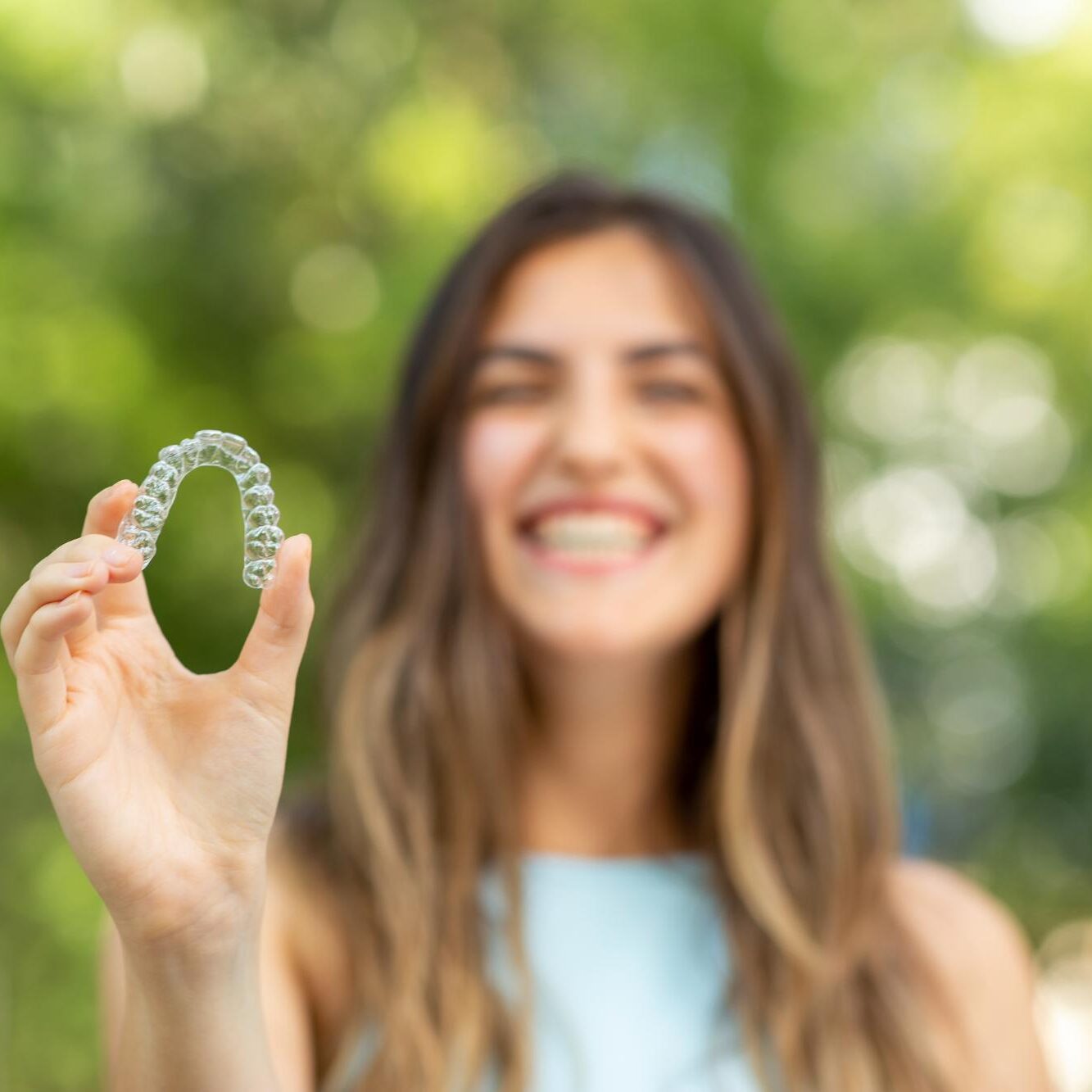 Young woman smiling outdoors holding a clear aligner